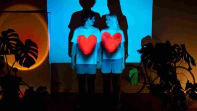 Boy and girl with red heart t-shirts, smiling in front of a digital screen.