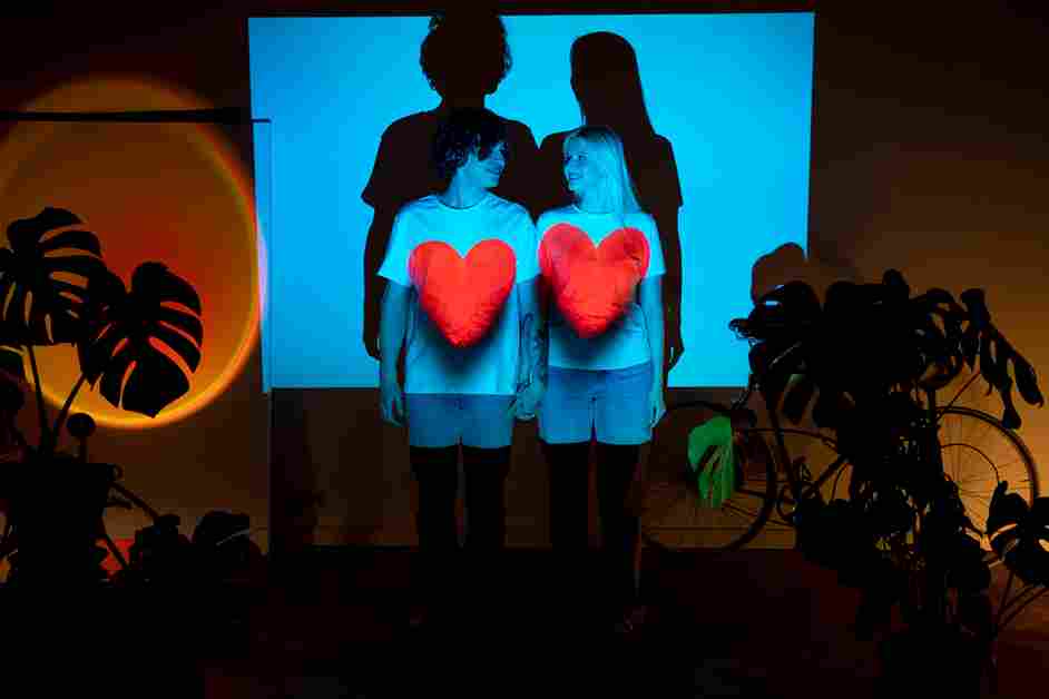 Boy and girl with red heart t-shirts, smiling in front of a digital screen.